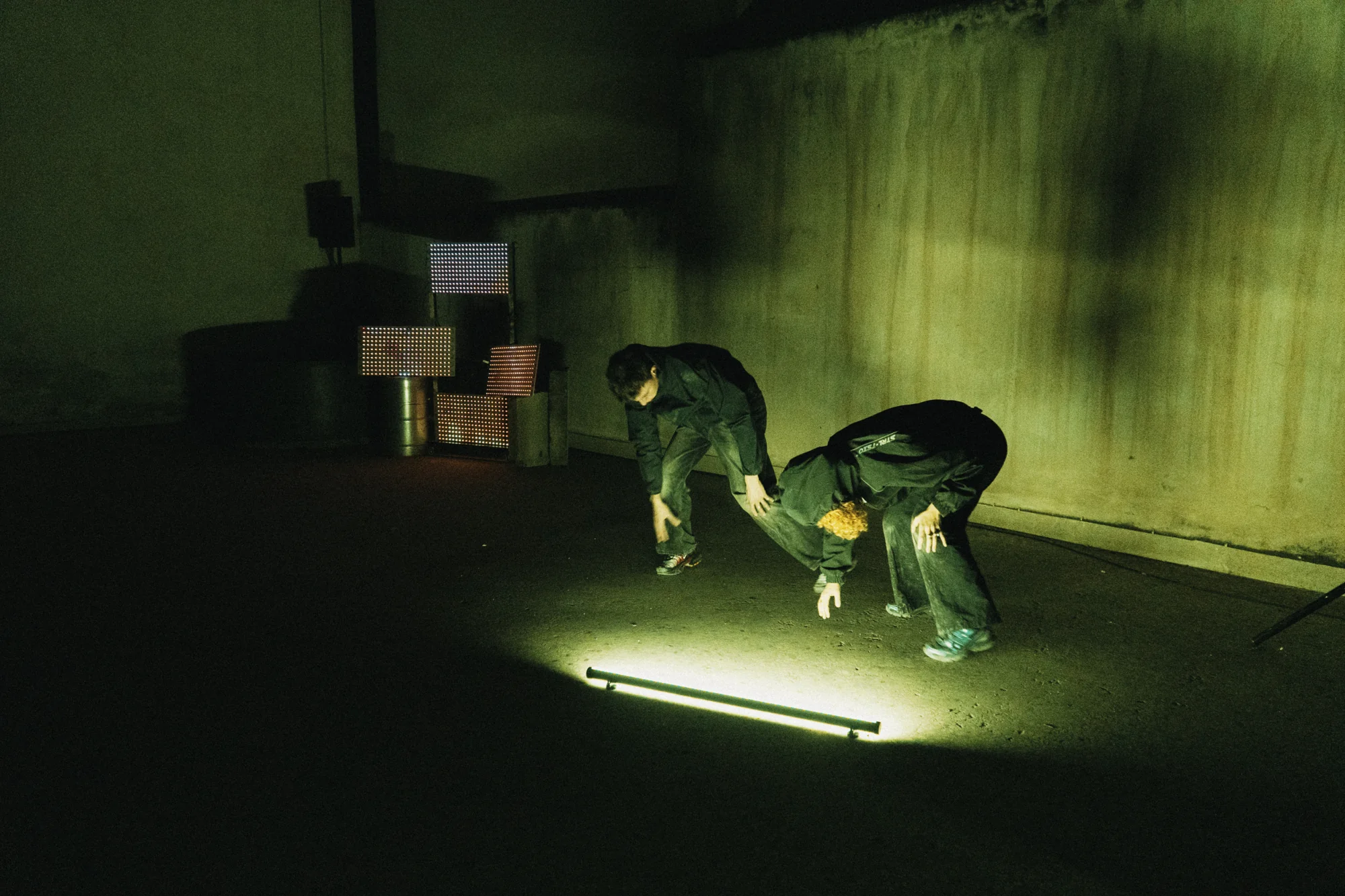 Two performers low to the ground beside a light tube, with the LED panels behind them.