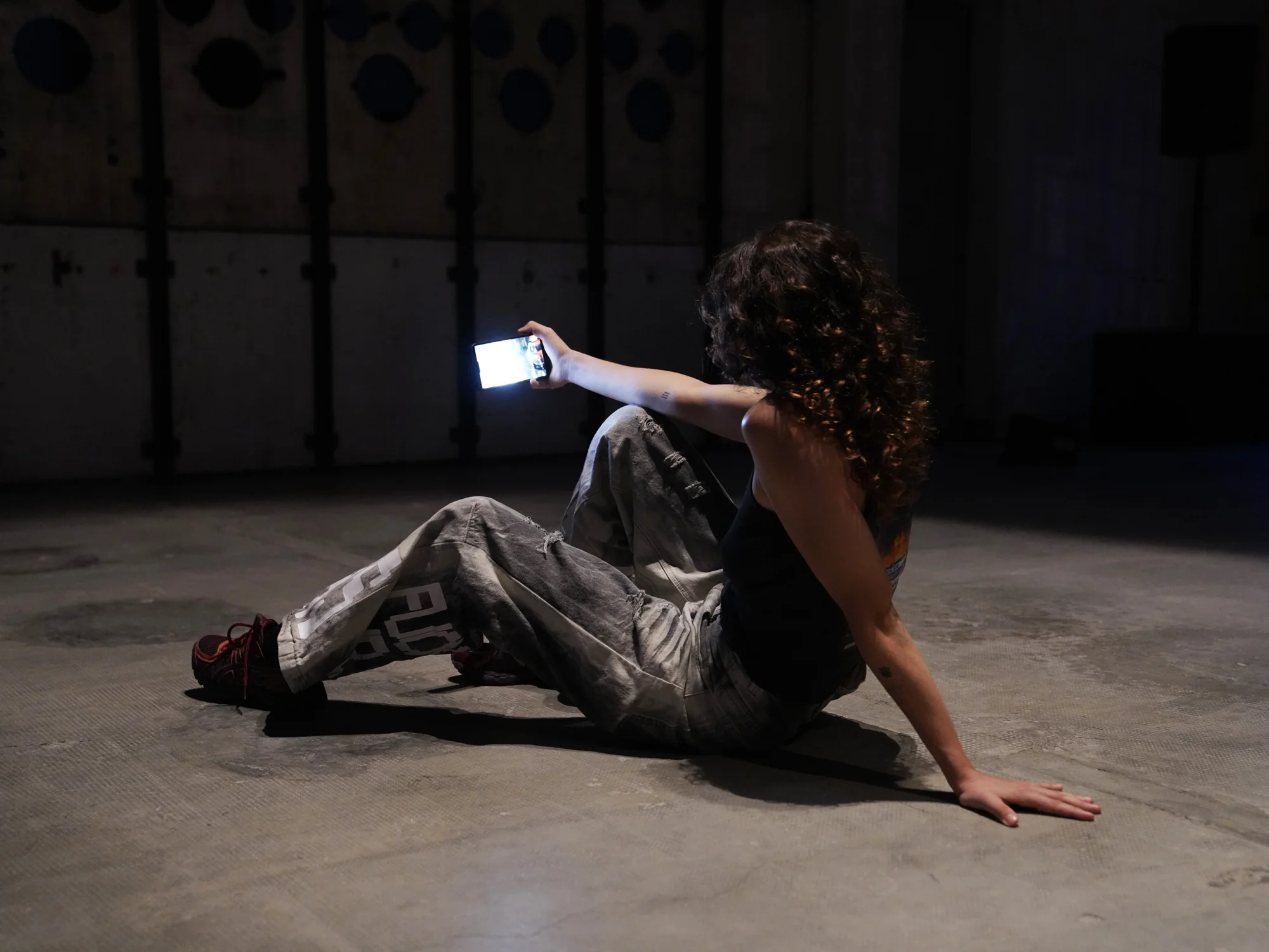 A performer seated on the floor holds the illuminated phone close to their face.