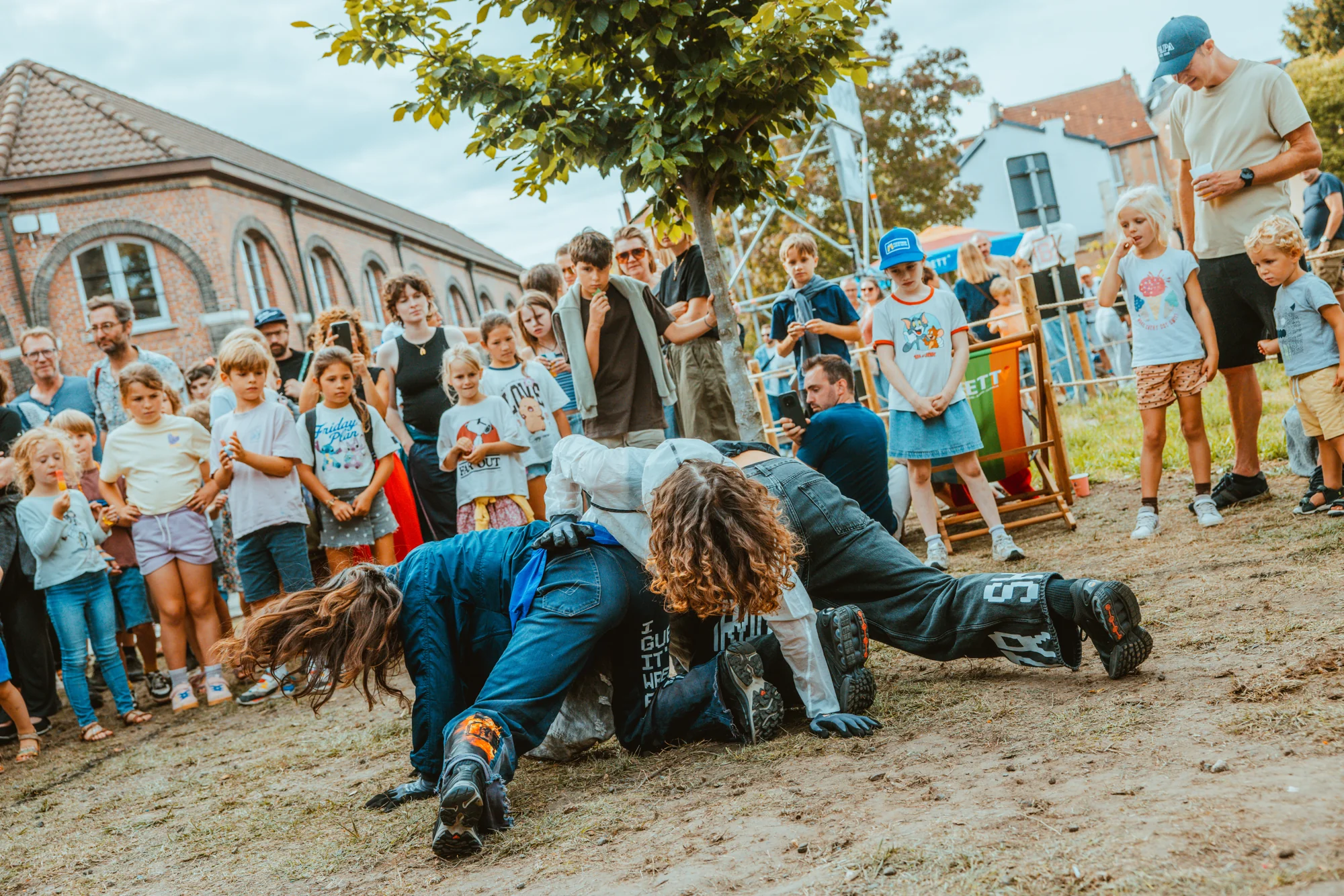 Three performers low to the ground, watched closely by the outdoor audience.